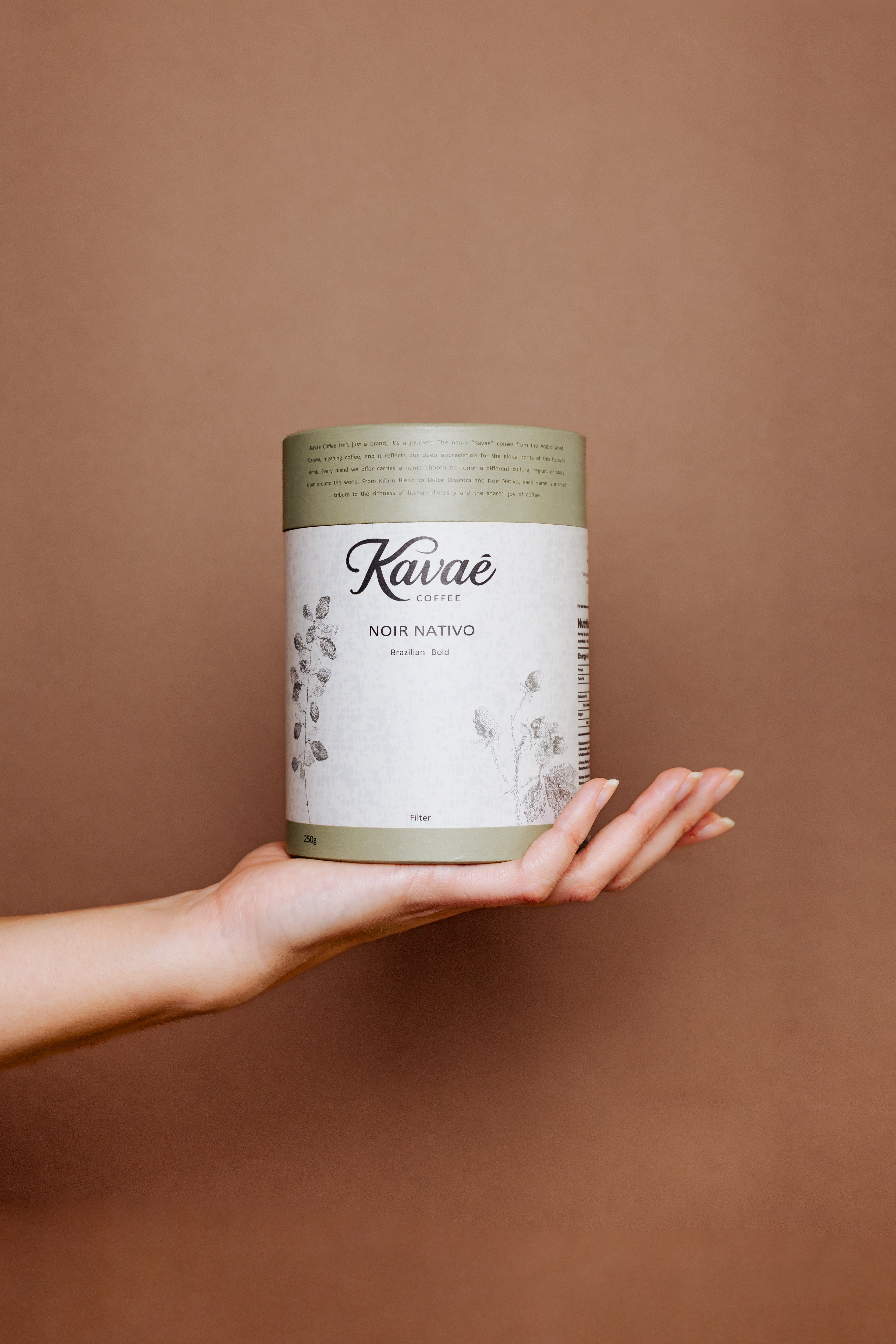 Hand holding a Kuváé coffee can against a brown background