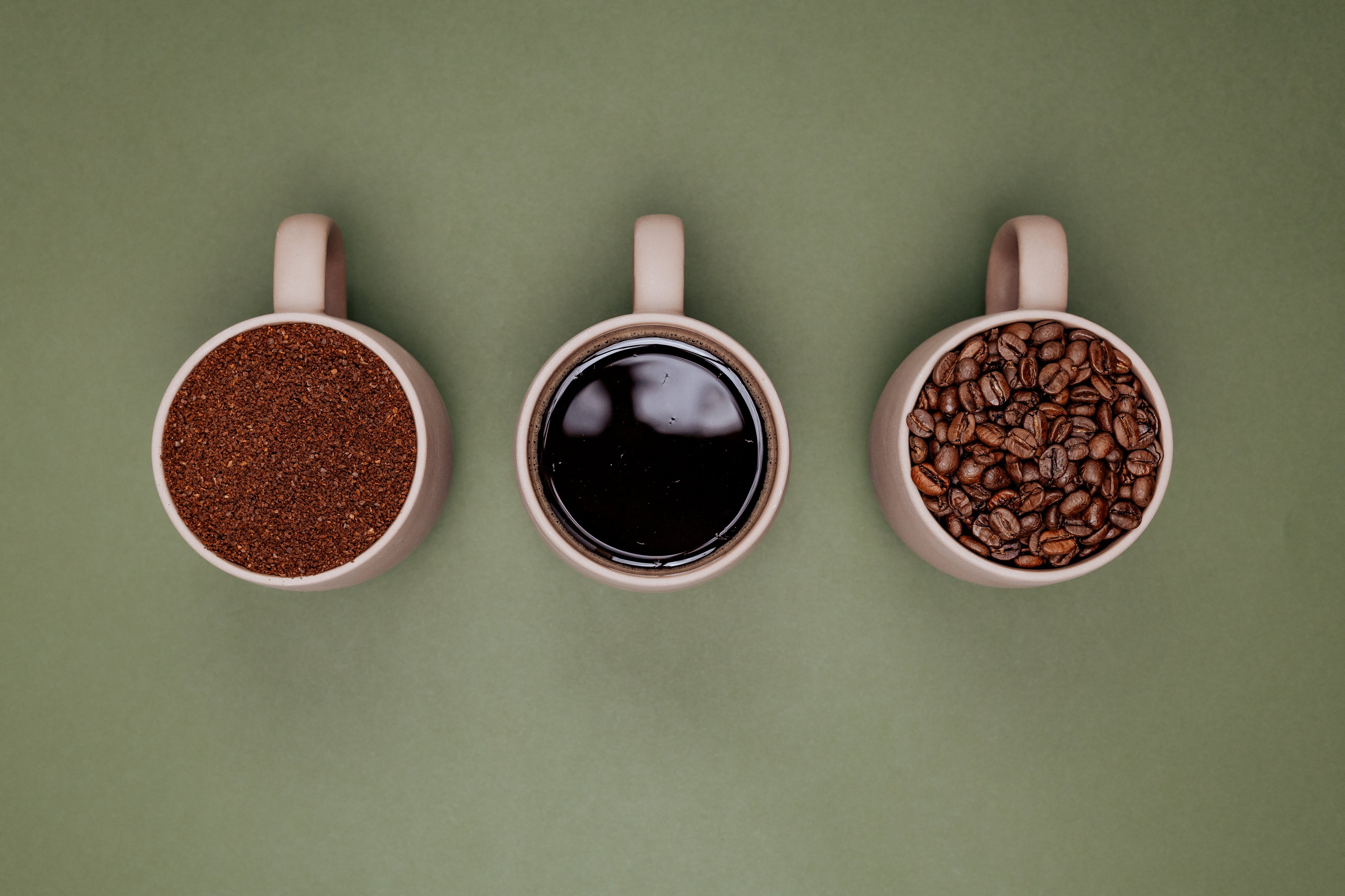 Three mugs with coffee and coffee beans on a green background